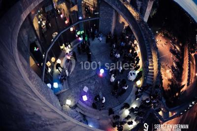 Façade vitrée d'un bâtiment moderne avec éclairages rouges, intégrée à des murs en pierre ancienne.