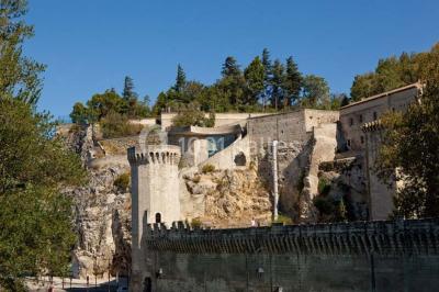 Façade vitrée d'un bâtiment moderne avec éclairages rouges, intégrée à des murs en pierre ancienne.