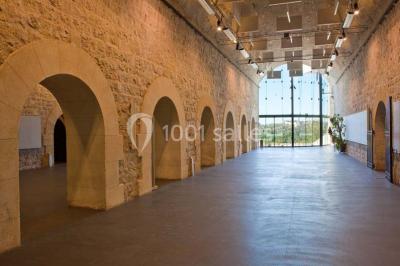 Façade vitrée d'un bâtiment moderne avec éclairages rouges, intégrée à des murs en pierre ancienne.