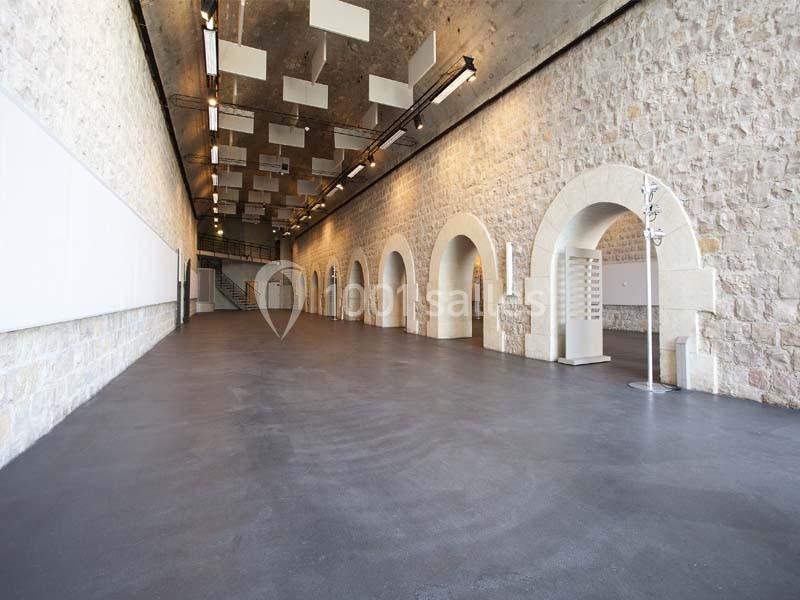 Salle spacieuse avec murs en pierre, arches et plafond équipé de panneaux acoustiques suspendus.