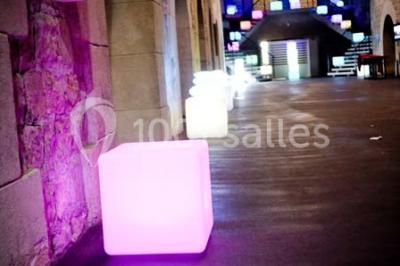 Façade vitrée d'un bâtiment moderne avec éclairages rouges, intégrée à des murs en pierre ancienne.