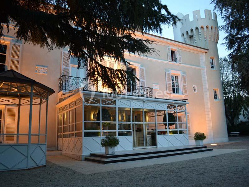Façade d'un bâtiment de style château avec une tour crénelée, éclairée à la tombée de la nuit.