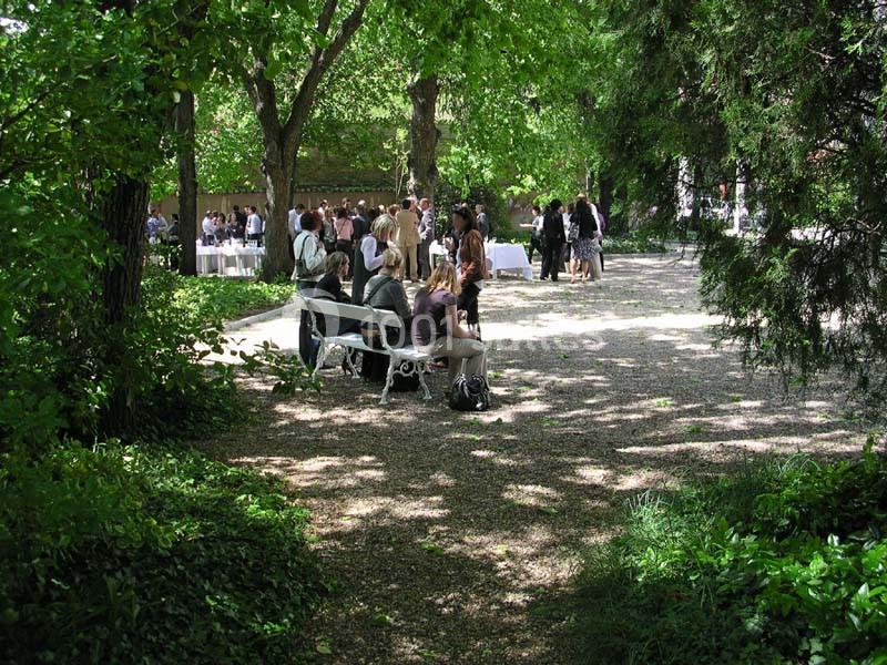 Personnes assises sur un banc et debout dans un jardin ombragé lors d'un événement en plein air.