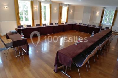 Salle de réunion avec parquet, chaises alignées, table avec projecteur et grandes fenêtres donnant sur l'extérieur.
