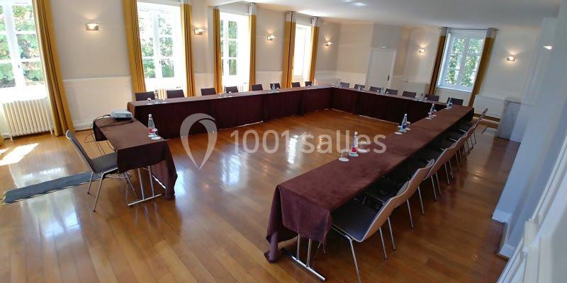 Salle de réunion lumineuse avec tables disposées en U, chaises alignées et grandes fenêtres donnant sur l'extérieur.