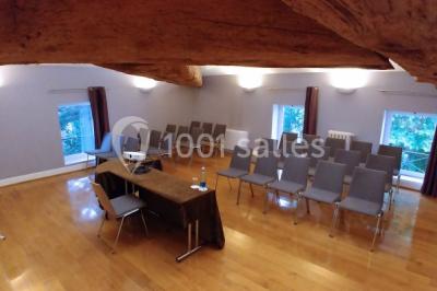 Salle de réunion avec parquet, chaises alignées, table avec projecteur et grandes fenêtres donnant sur l'extérieur.