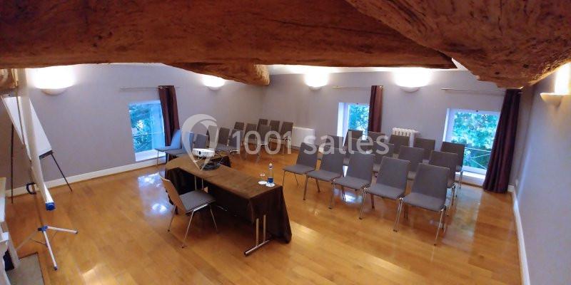 Salle de réunion avec parquet, chaises alignées, table avec projecteur et grandes fenêtres donnant sur l'extérieur.