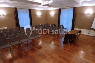 Salle de réunion avec parquet, chaises alignées, table avec projecteur et grandes fenêtres donnant sur l'extérieur.