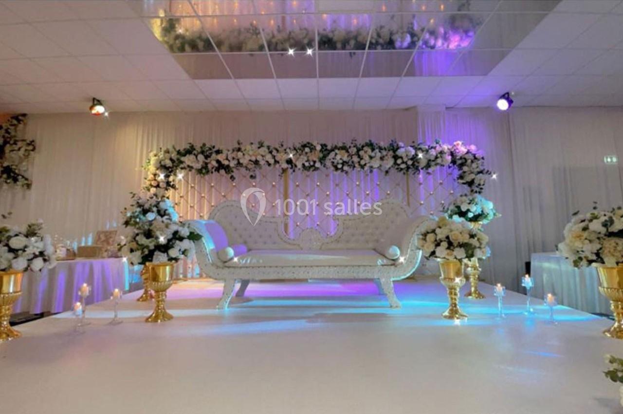 Canapé blanc décoratif entouré de fleurs blanches et dorées sur une scène éclairée de lumières colorées.