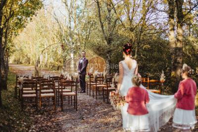 Terrasse en bois ombragée avec des tonneaux en guise de tables, surplombant un plan d'eau entouré de végétation.