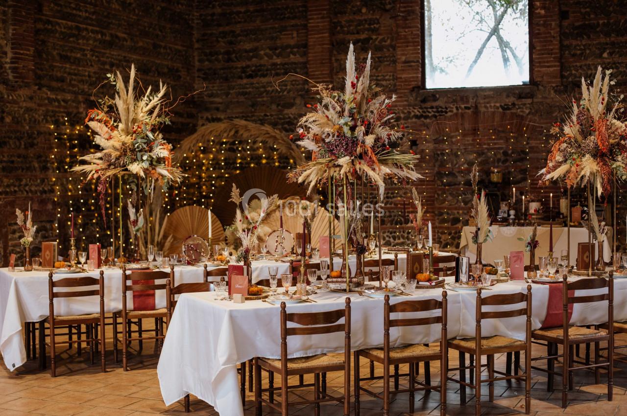 Salle de réception décorée avec des tables dressées, des compositions florales et des lumières suspendues.
