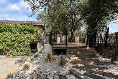 Terrasse en bois ombragée avec des tonneaux en guise de tables, surplombant un plan d'eau entouré de végétation.