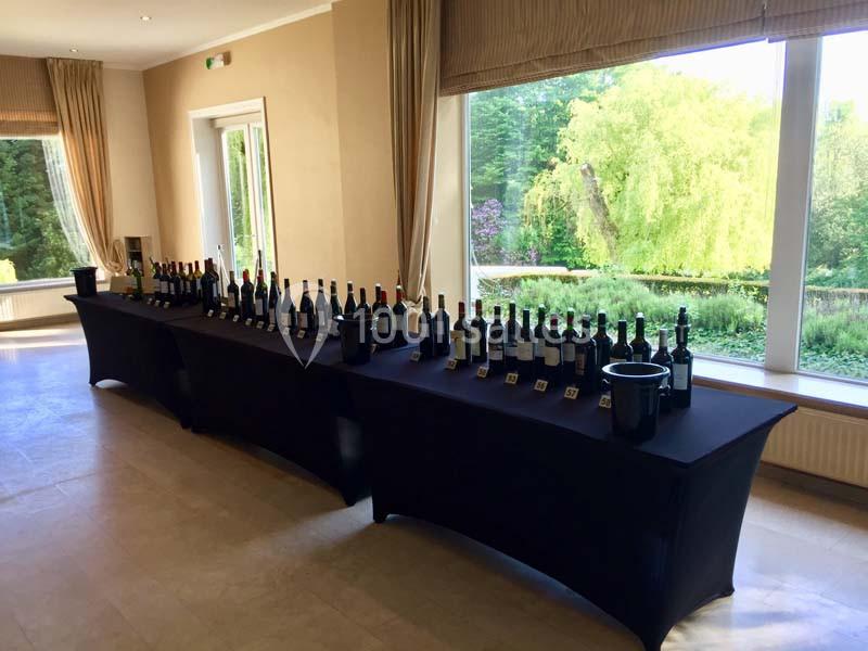Table couverte de nappes noires présentant des bouteilles de vin alignées devant de grandes fenêtres donnant sur un jardin.