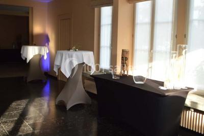 Salle de réception avec tables rondes dressées, nappes blanches, assiettes dorées et décoration florale centrale.