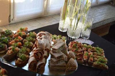 Salle de réception avec tables rondes dressées, nappes blanches, assiettes dorées et décoration florale centrale.
