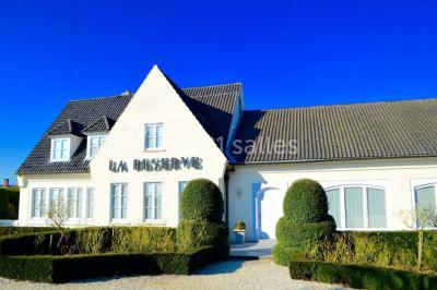 Salle de réception avec tables rondes dressées, nappes blanches, assiettes dorées et décoration florale centrale.
