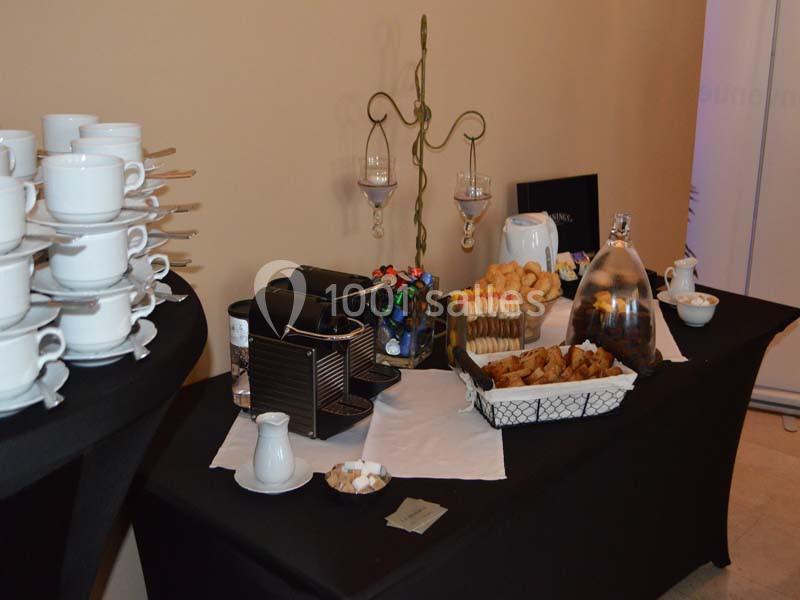 Table de buffet avec machine à café, tasses empilées, viennoiseries, carafe d'eau et accessoires.