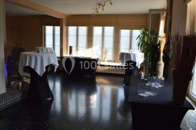 Salle de réception avec tables rondes dressées, nappes blanches, assiettes dorées et décoration florale centrale.