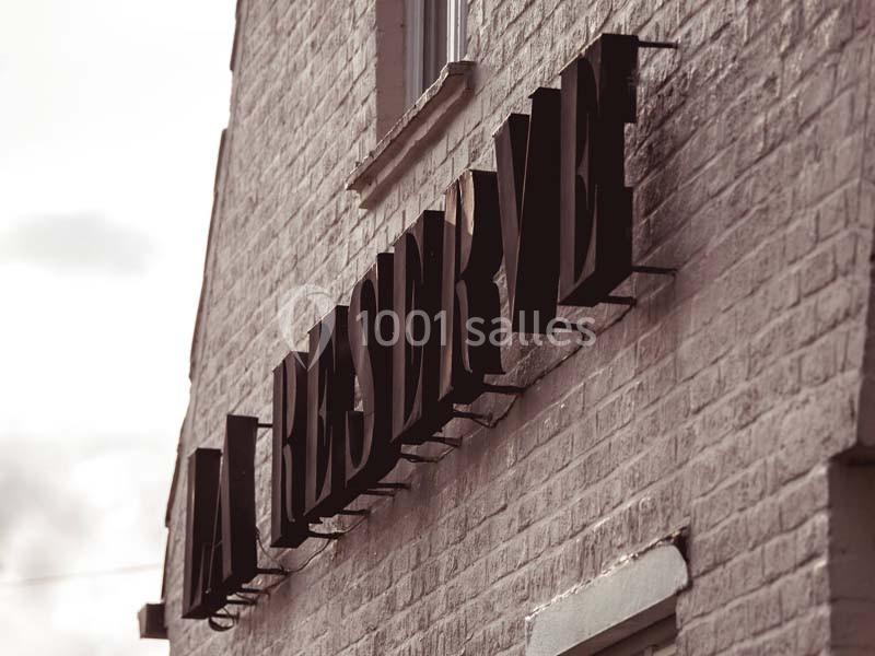 Enseigne en lettres noires indiquant ’La Réserve’ fixée sur un mur en briques claires.