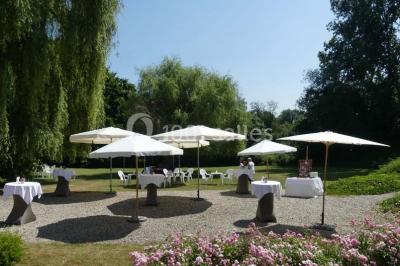 Salle de réception avec tables rondes dressées, nappes blanches, assiettes dorées et décoration florale centrale.