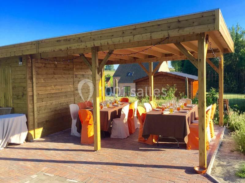 Pergola en bois sur une terrasse pavée, aménagée avec des tables dressées et des chaises décorées pour un repas extérieur.