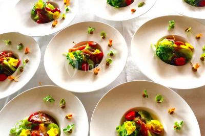 Salle de réception avec tables rondes dressées, nappes blanches, assiettes dorées et décoration florale centrale.