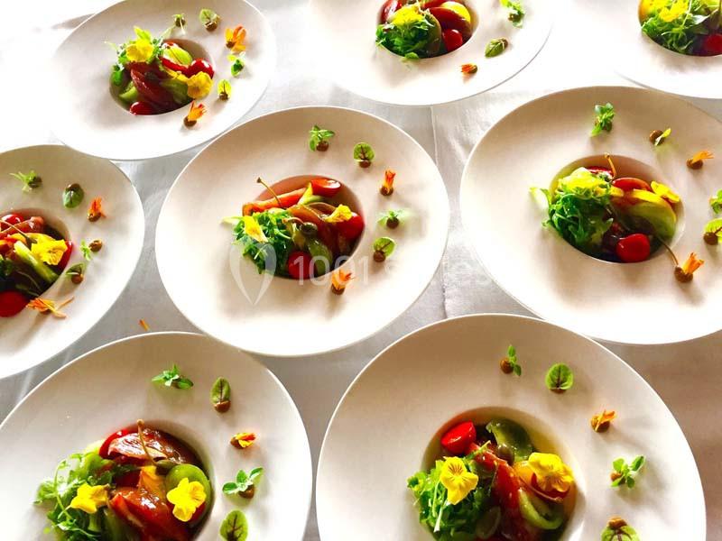 Assiettes blanches garnies de salades colorées, fleurs comestibles et légumes variés, disposées sur une table blanche.