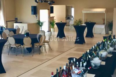 Salle de réception avec tables rondes dressées, nappes blanches, assiettes dorées et décoration florale centrale.