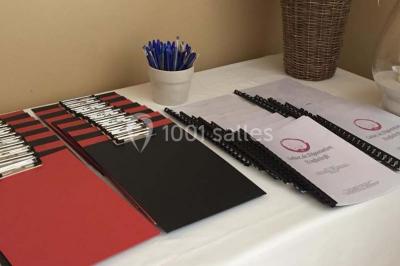 Salle de réception avec tables rondes dressées, nappes blanches, assiettes dorées et décoration florale centrale.