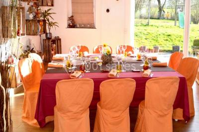 Salle de réception avec tables rondes dressées, nappes blanches, assiettes dorées et décoration florale centrale.