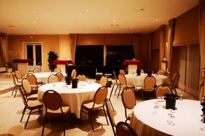 Salle de réception avec tables rondes dressées, nappes blanches, assiettes dorées et décoration florale centrale.