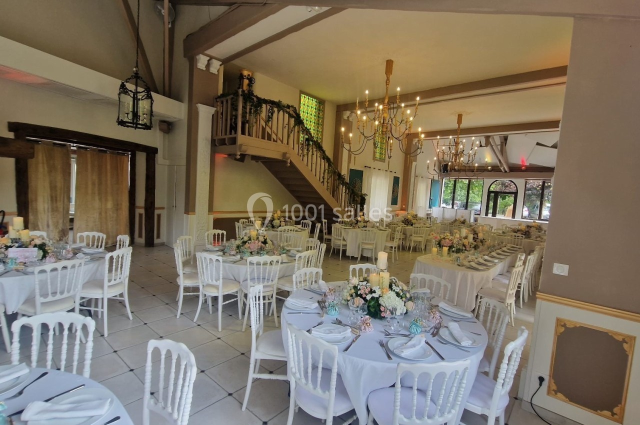 Salle de réception décorée avec des tables rondes, nappes blanches, chaises assorties et arrangements floraux.