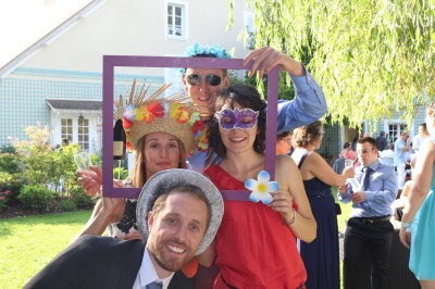 Miniature Location salle Tigeaux (Seine-et-Marne) - Le Manoir de Tigeaux #34 Des personnes souriantes posent avec des accessoires festifs et un cadre violet dans un jardin ensoleillé.