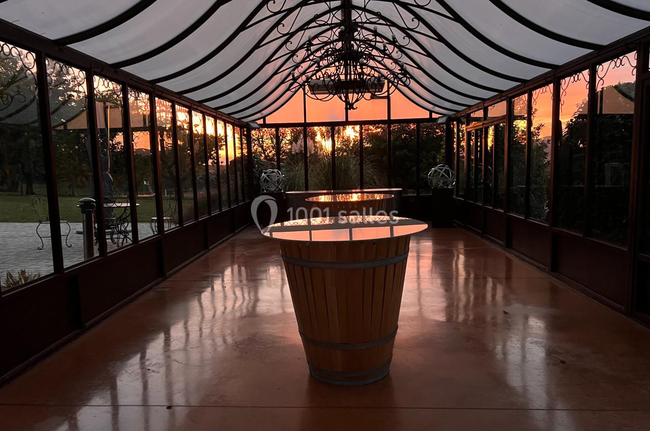 Intérieur d'une serre vitrée au coucher du soleil, avec une table en tonneau au centre et un sol brillant.