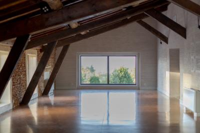 Vue intérieure d'une pièce mansardée lumineuse avec poutres apparentes, sol en bois et une grande fenêtre donnant sur des…