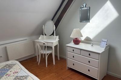 Miniature Location salle Aunou-sur-Orne (Orne) - Le Domaine de La Cour #14 Chambre mansardée avec coiffeuse blanche, chaise, commode assortie, miroir et lumière naturelle provenant d'une fenêtre.