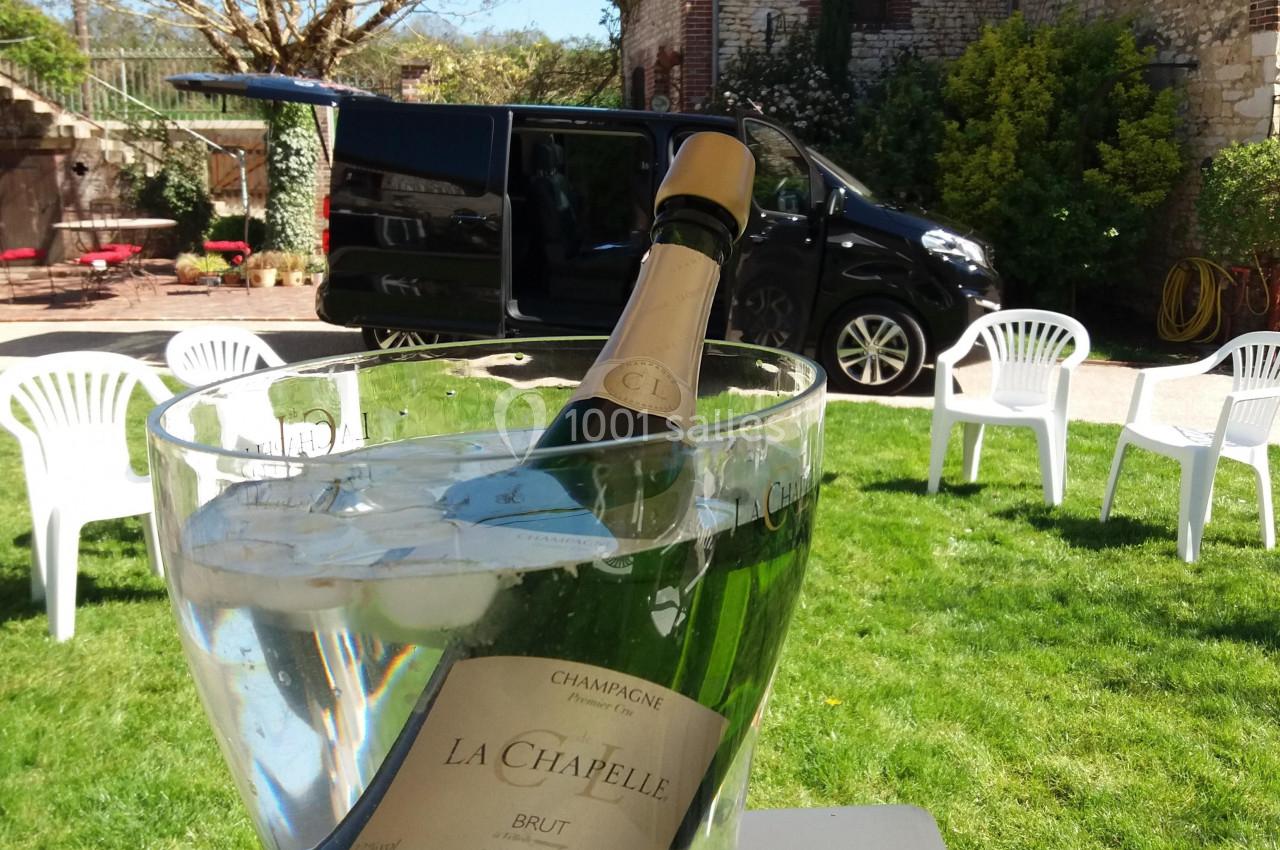 Bouteille de champagne dans un seau transparent rempli d'eau, posée sur une table dans un jardin ensoleillé.