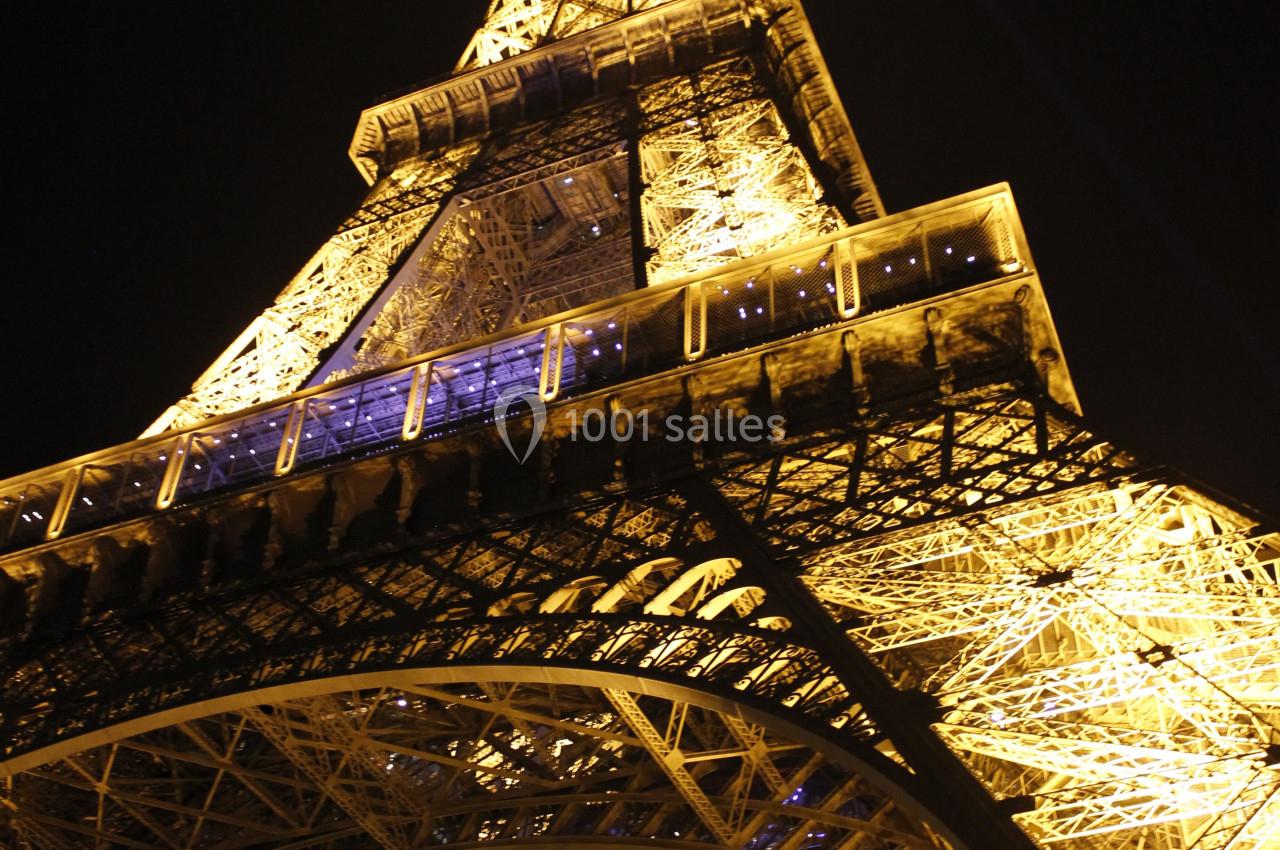 Vue en contre-plongée de la tour Eiffel illuminée la nuit, mettant en valeur sa structure métallique.