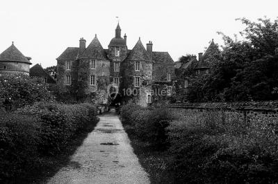 Façade d'un grand bâtiment ancien entouré de verdure, avec plusieurs véhicules stationnés devant.