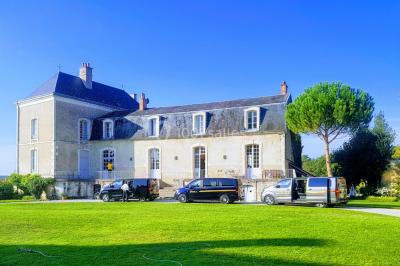 Façade d'un grand bâtiment ancien entouré de verdure, avec plusieurs véhicules stationnés devant.