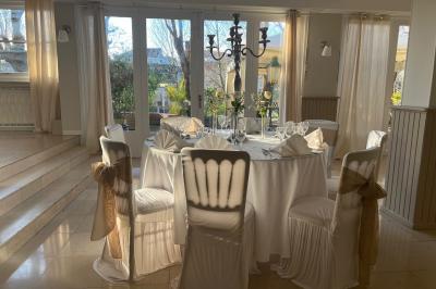 Salle lumineuse avec table ronde dressée pour un repas, nappes blanches et chaises décorées de rubans beiges.