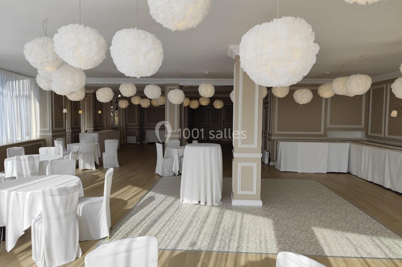 Salle de réception lumineuse avec tables et chaises recouvertes de housses blanches, décorée de suspensions en papier.