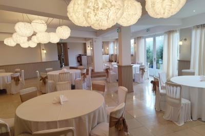 Salle lumineuse avec table ronde dressée pour un repas, nappes blanches et chaises décorées de rubans beiges.