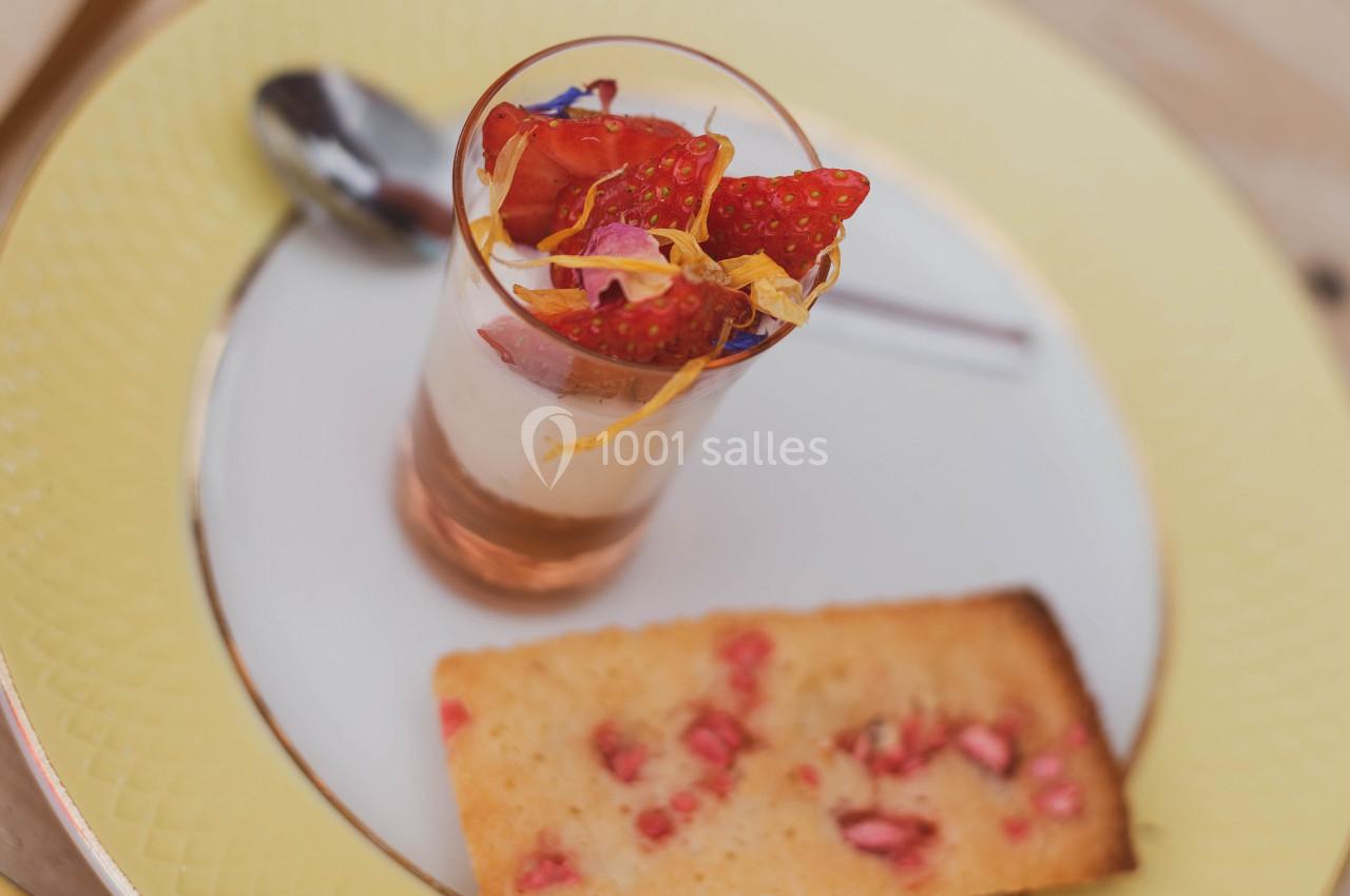 Verrine de dessert avec mousse blanche, fraises et fleurs comestibles, accompagnée d'un biscuit aux éclats de fruits.