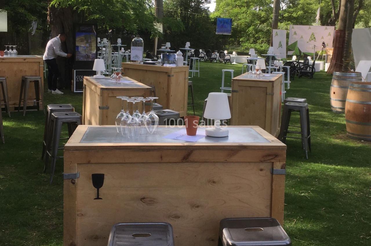 Tables en bois avec tabourets, verres et lampes disposées sur une pelouse pour un événement en plein air.