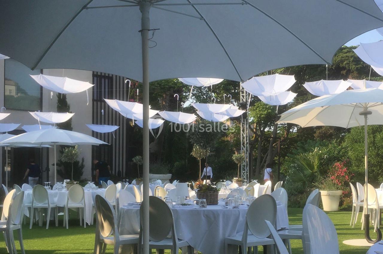 Tables dressées en extérieur sous des parasols blancs, avec des parapluies suspendus en décoration.
