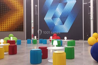 Salle décorée pour un événement avec des tables hautes éclairées et des lumières colorées en arrière-plan.