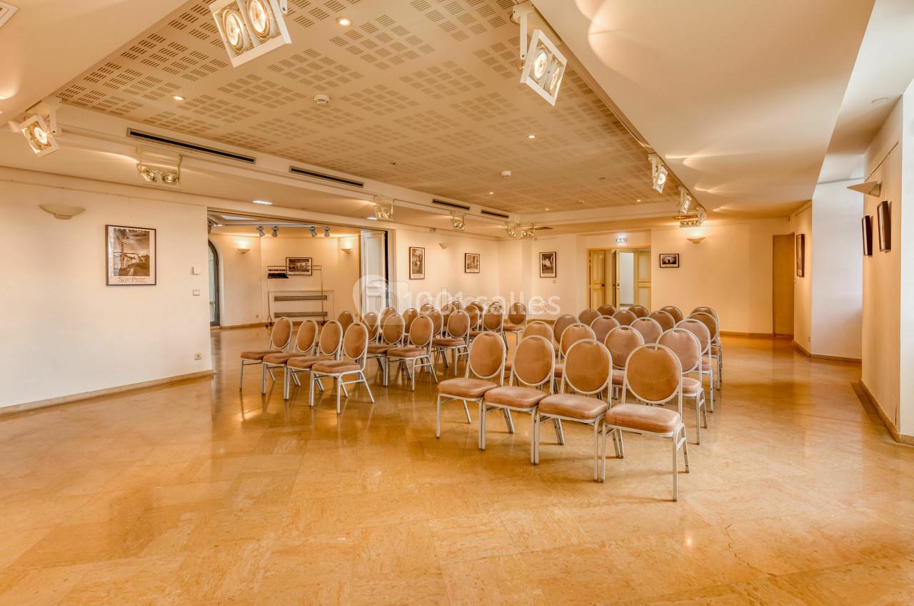 Salle de conférence lumineuse avec rangées de chaises beige disposées face à un espace vide, murs ornés de cadres.