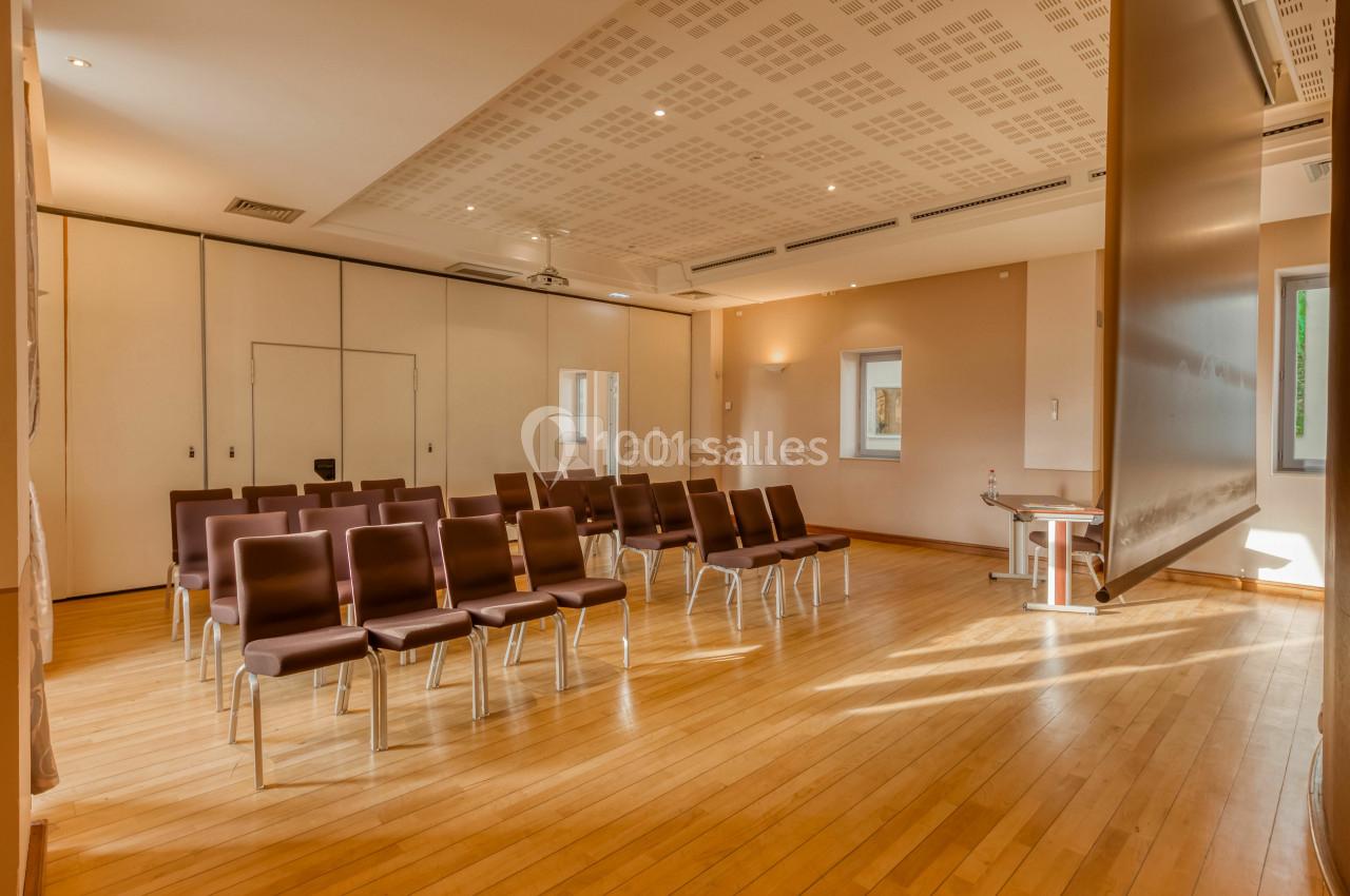 Salle de réunion lumineuse avec parquet en bois, chaises alignées et cloisons modulables.