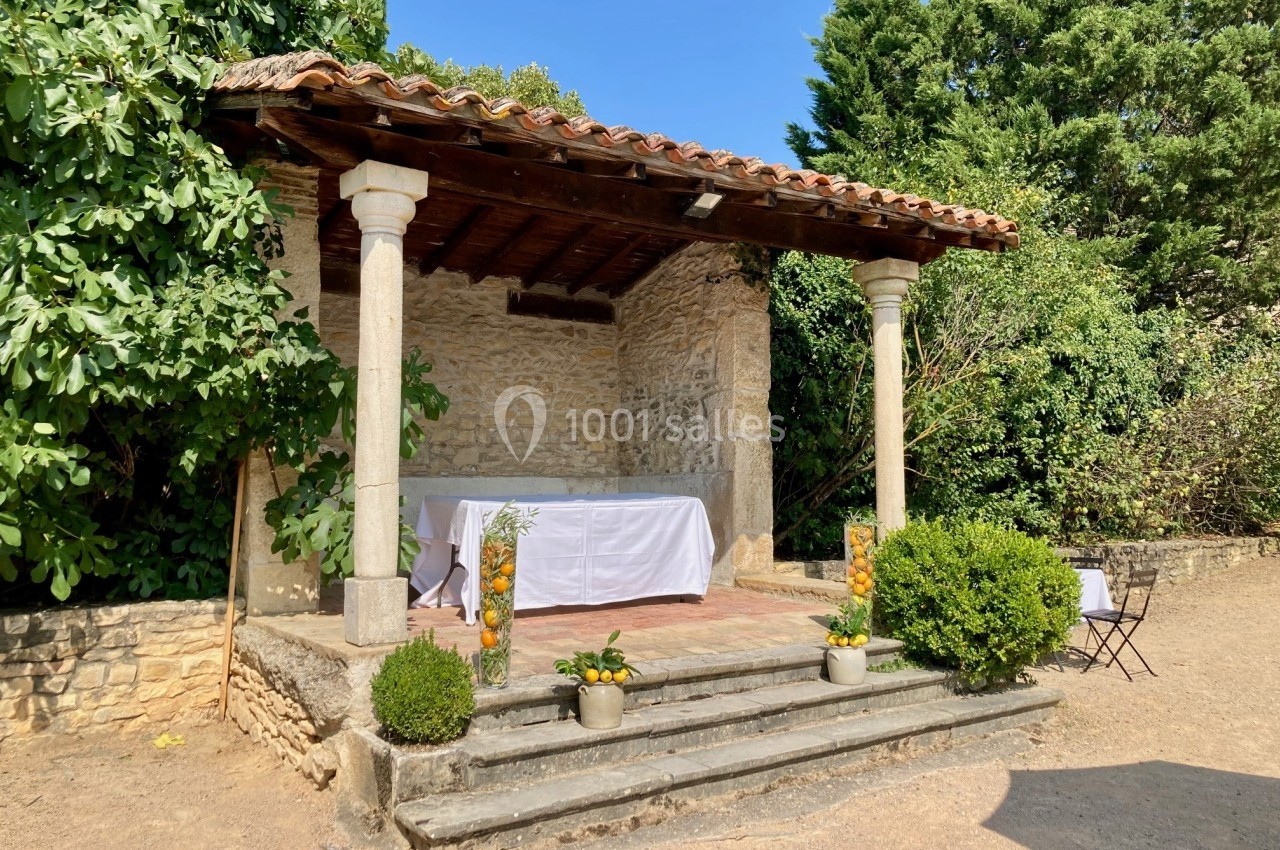 Petit autel en pierre avec toit en tuiles, entouré de végétation, décoré de plantes et d'une table recouverte d'une nappe…
